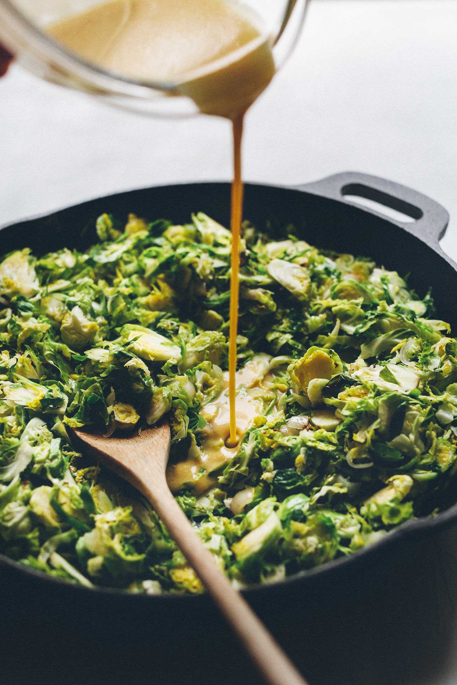 Pouring dressing over warm Brussels Sprouts in a cast-iron skillet