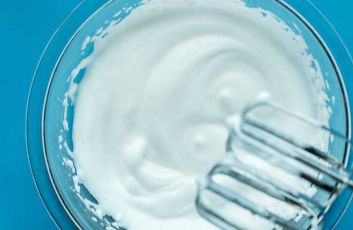 Electric mixer blades over a bowl of freshly whipped aquafaba