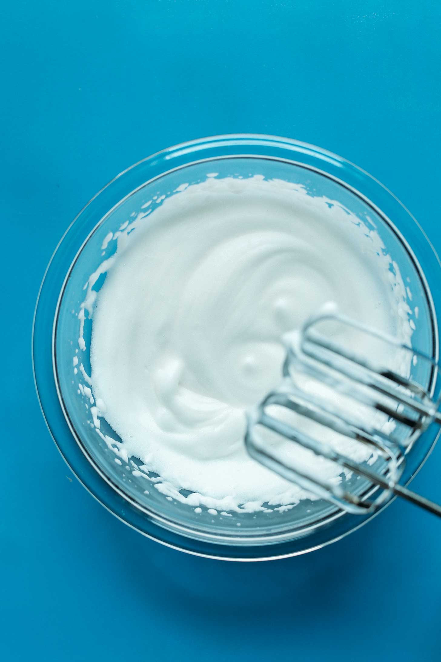 Electric mixer blades over a bowl of freshly whipped aquafaba