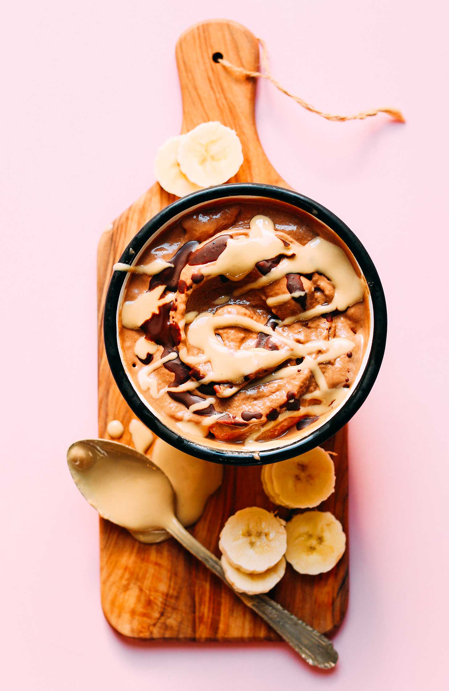 Wood cutting board with a bowl of vegan Chocolate Tahini Banana Soft Serve
