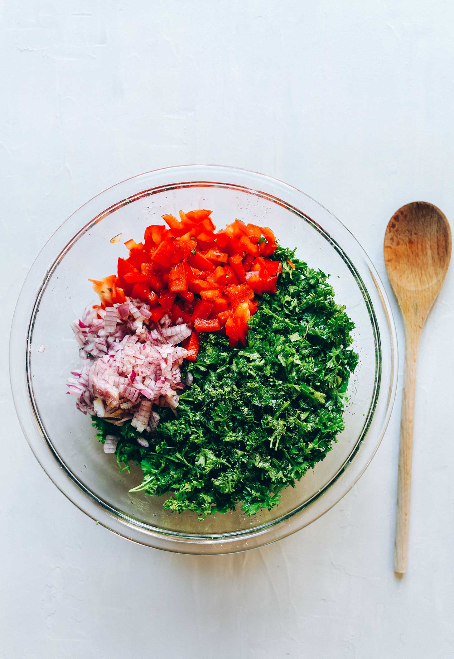 Glass bowl with fresh bell peppers, red onion, and parsley for making gluten-free Tabbouleh Salad