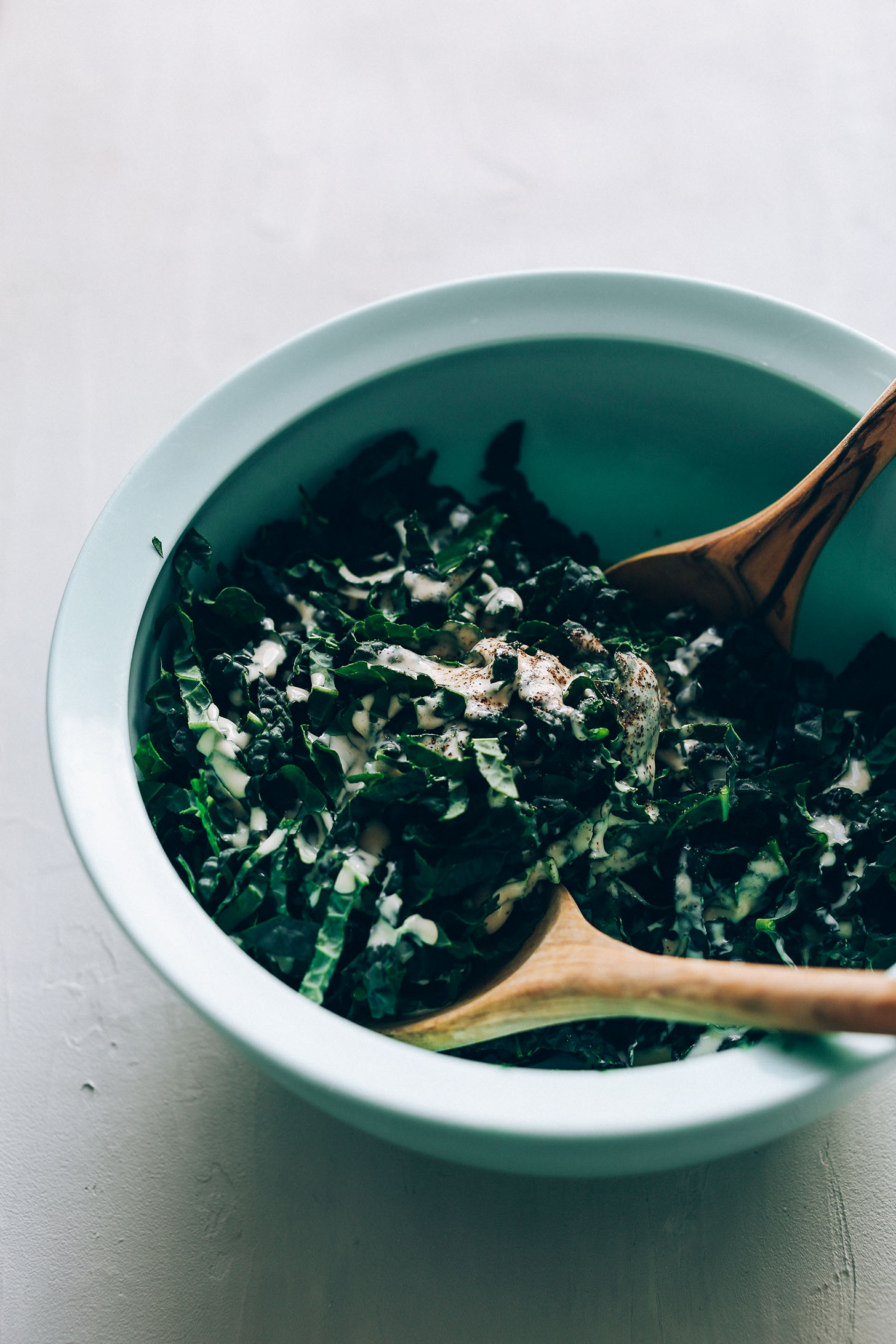 Using wooden spoons to toss shredded kale with tahini dressing
