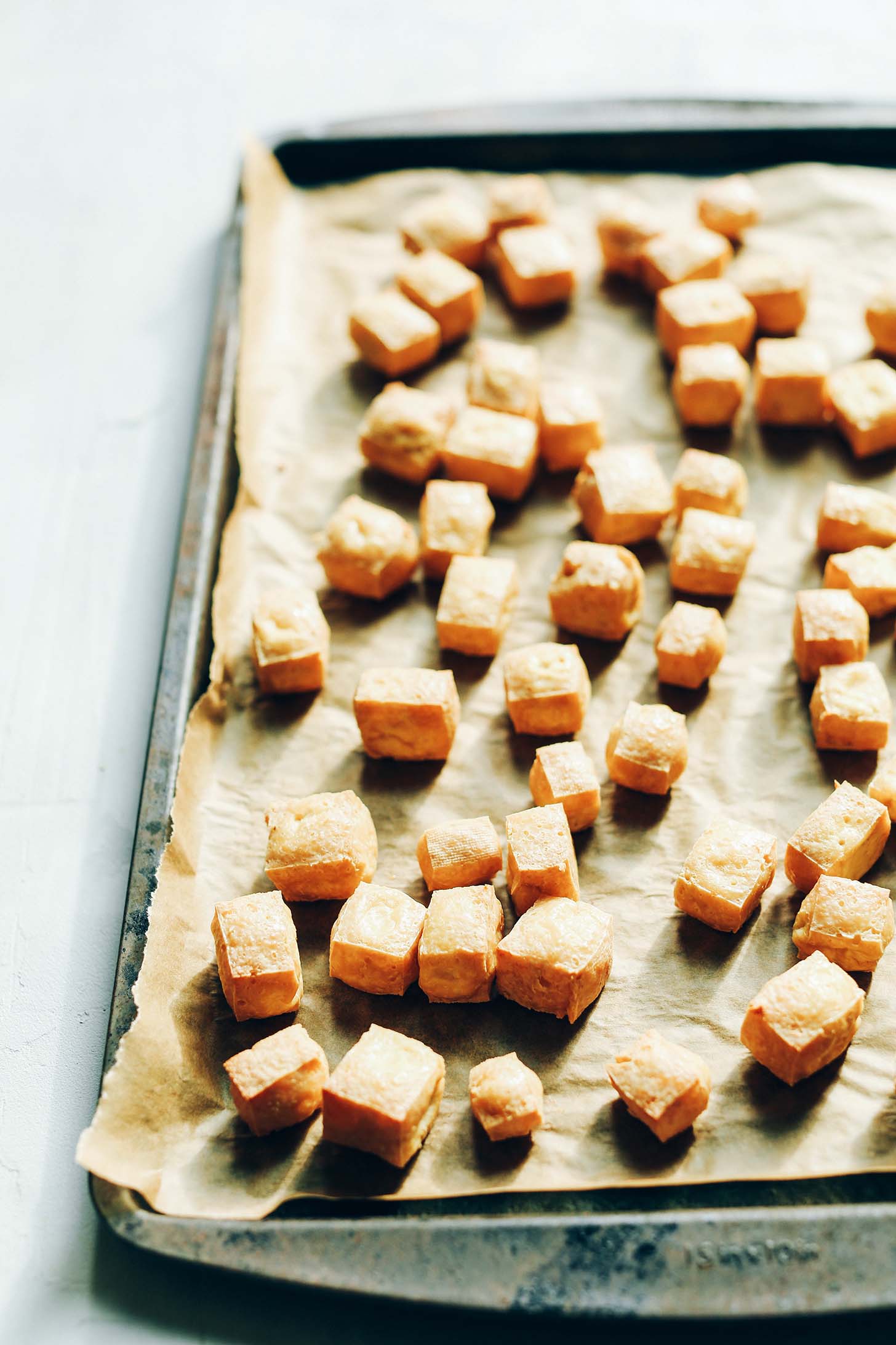 Parchment-lined baking sheet with cubed tofu for making gluten-free vegan Almond Butter Tofu Stir Fry