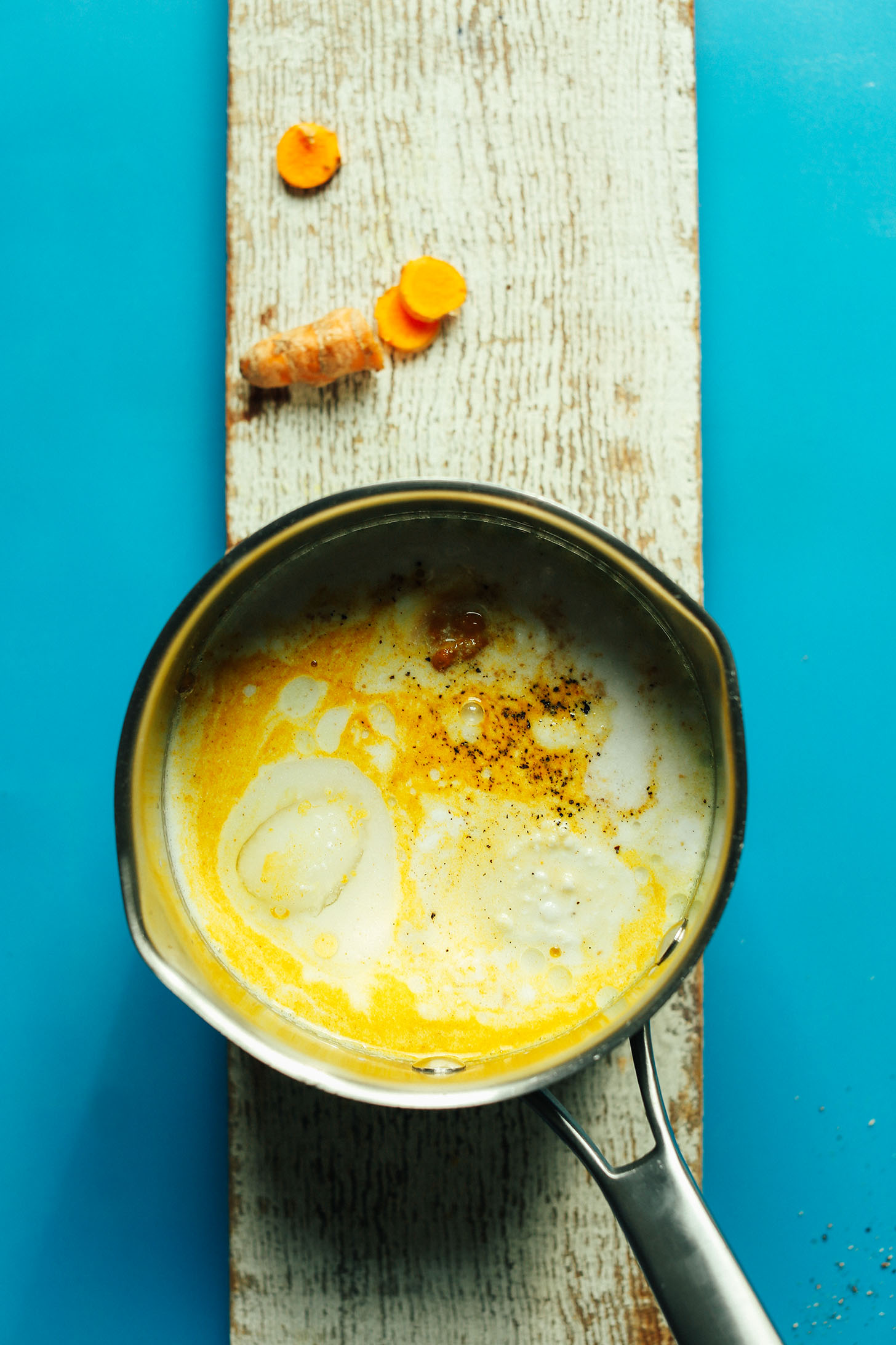 Colorful mug of Creamy Vegan Golden milk displayed on a wood plank with fresh turmeric