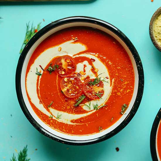 Bowl of Creamy Red Pepper Tomato Soup with fresh dill, roasted cherry tomatoes, and coconut milk