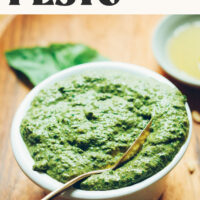 Spoon in a bowl of homemade vegan pesto with text above it that readers creamy + garlicky 5-minute easy vegan pesto