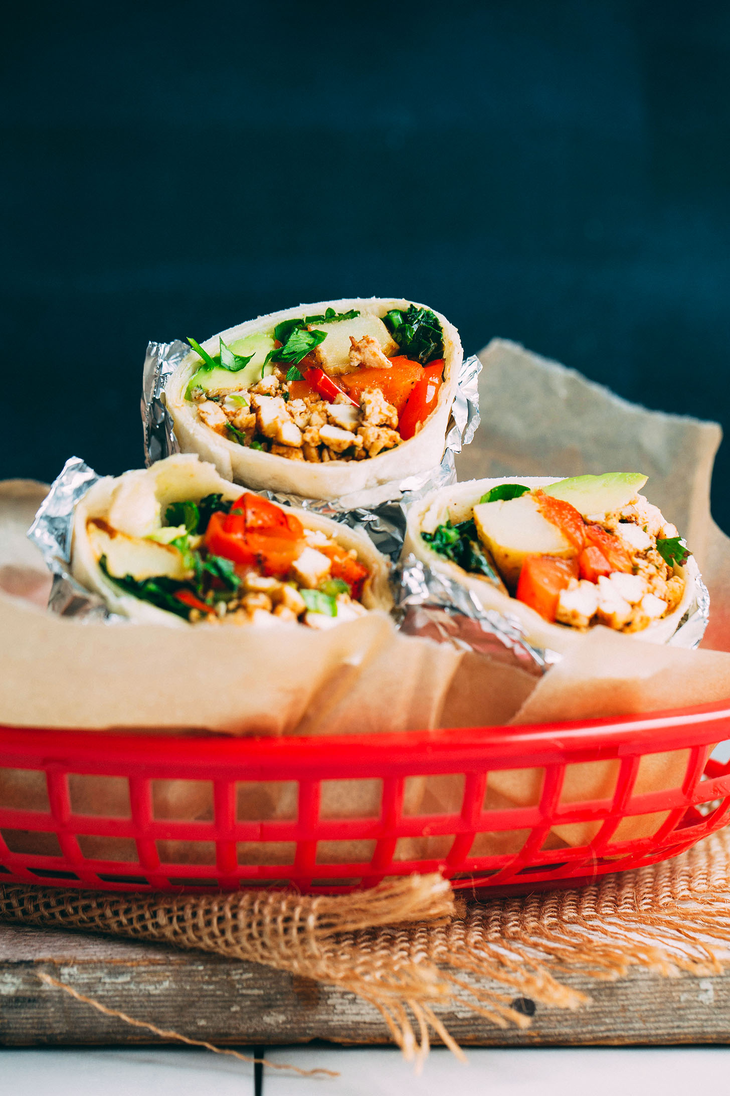 Three Vegan Breakfast Burritos wrapped in tin foil and displayed in a red basket