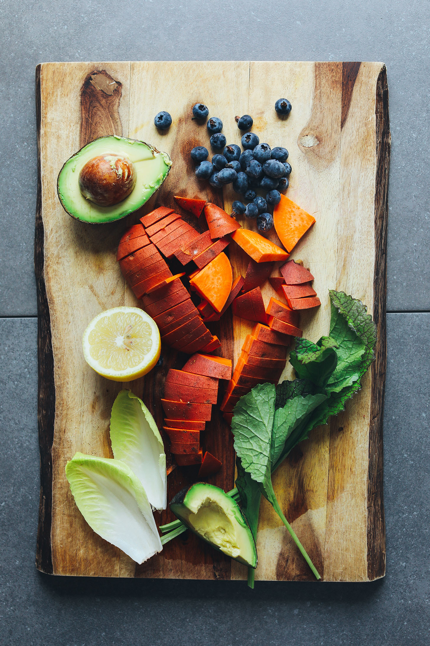 Wood cutting board featuring avocado, blueberries, sweet potato, lemon, endive, and mustard greens for a Vegan Breakfast Salad