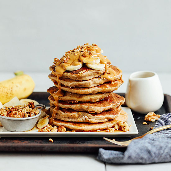 Platter with a stack of Banana Pancakes topped with banana slices, peanut butter, and granola