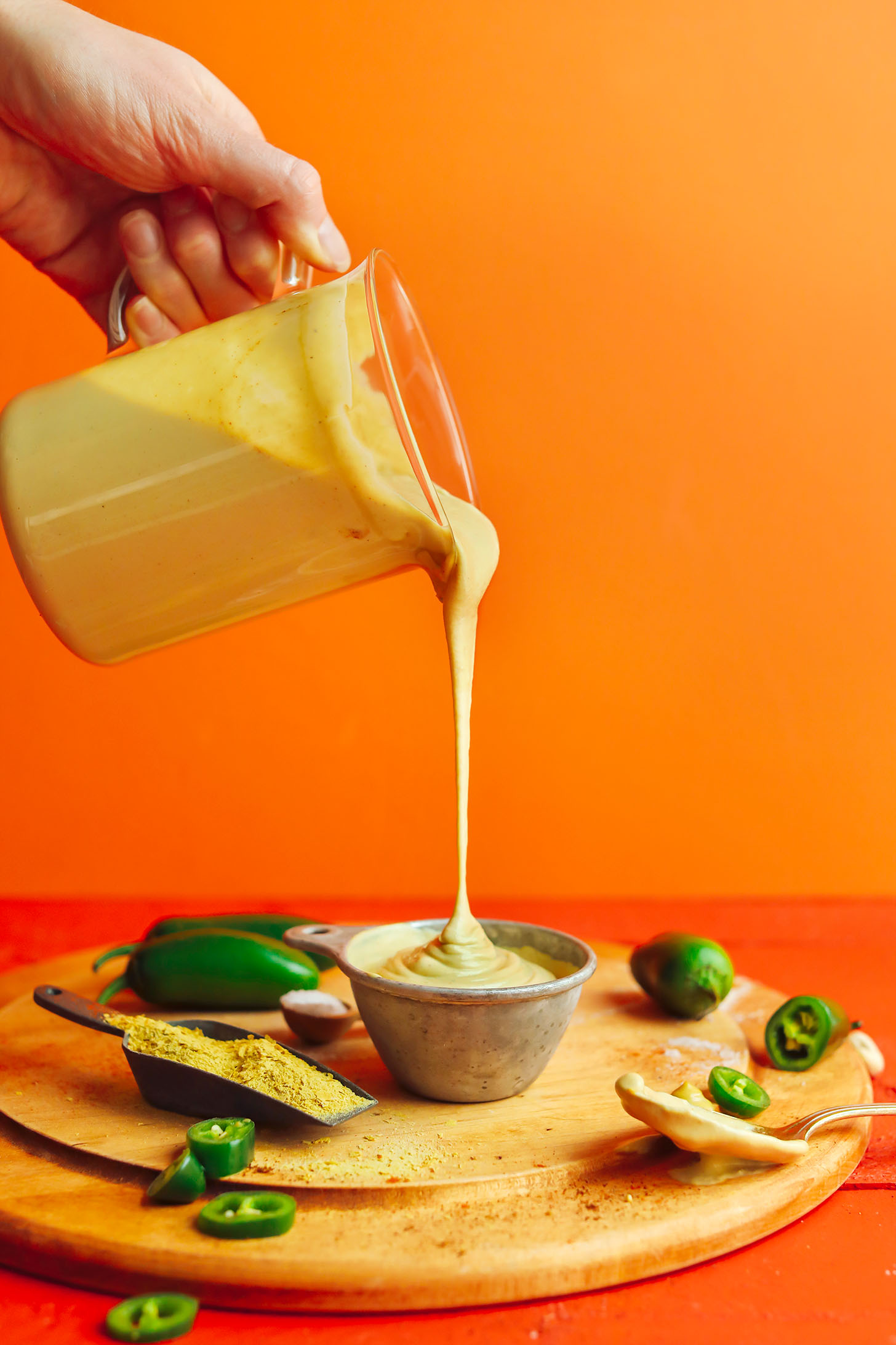 Pouring Roasted Jalapeno Vegan Queso Cheese dip into a measuring cup