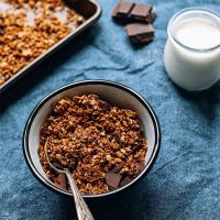 Bowl and tray of Chocolate Sea Salt Granola beside a small jar of dairy-free milk