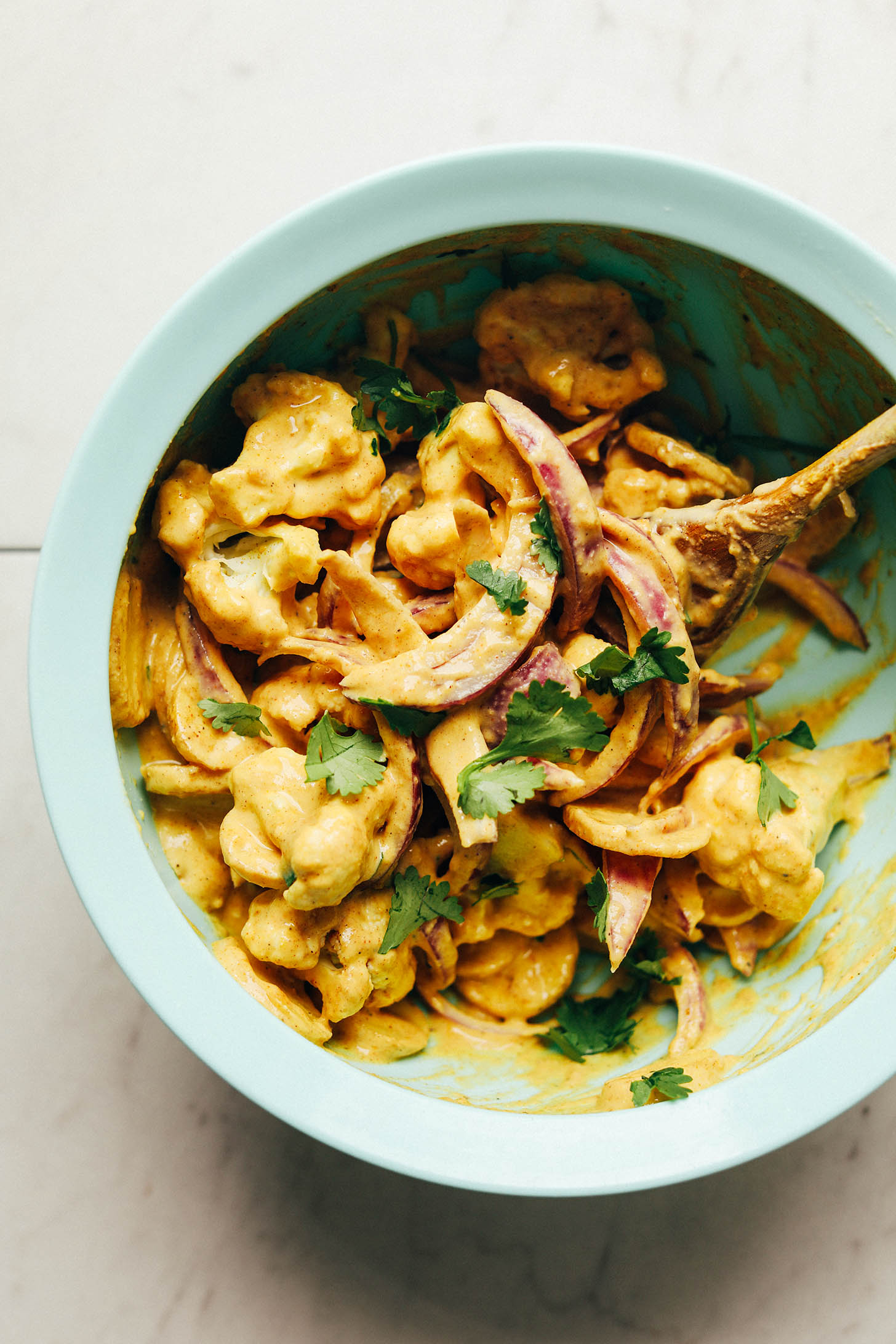 Using a wooden spoon to coat vegetables with sauce for plant-based Vegetable Pakoras