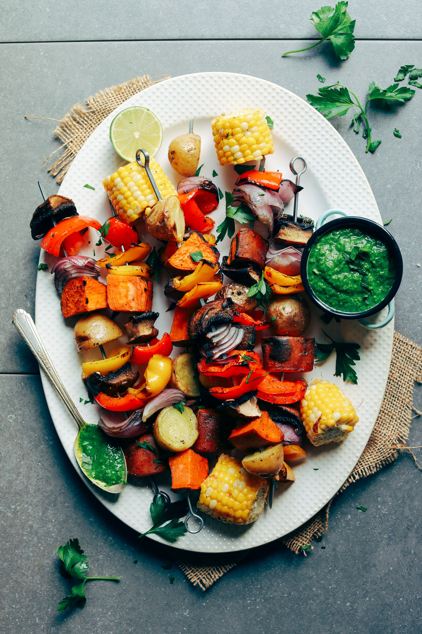 Metal skewers loaded with freshly grilled vegetables with sides of lime and fresh chimichurri