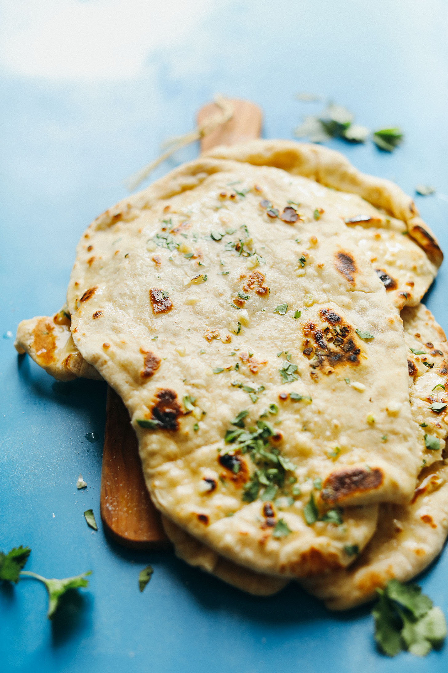 Vegan Naan flatbreads stacked on a wood cutting board and sprinkled with fresh cilantro