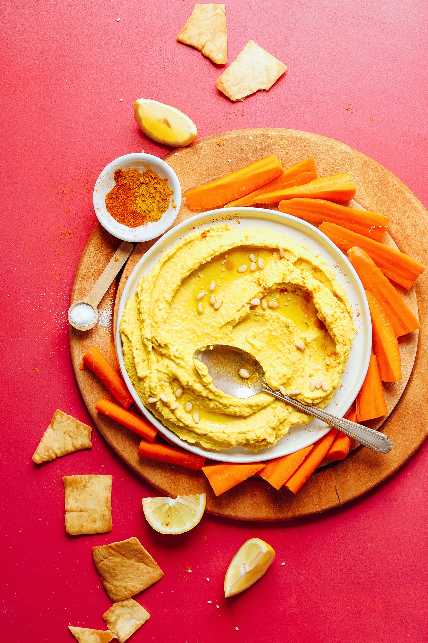Wood cutting board featuring a bowl of our homemade hummus packed with anti-inflammatory spices and served with carrot sticks