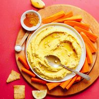 Bowl of Golden Goddess Turmeric Hummus surrounded by carrot sticks