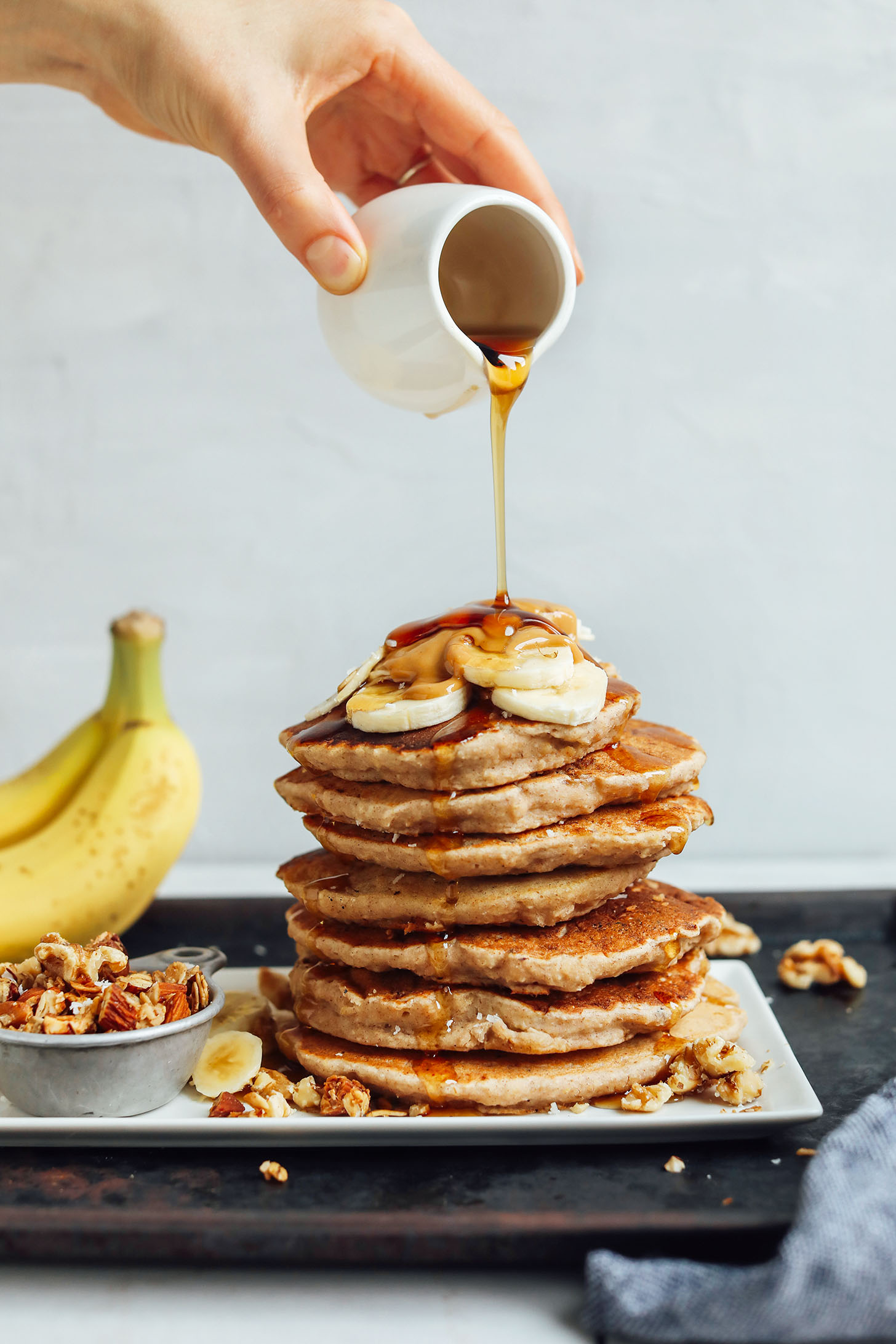 Drizzling syrup onto a stack of gluten-free vegan Banana Pancakes