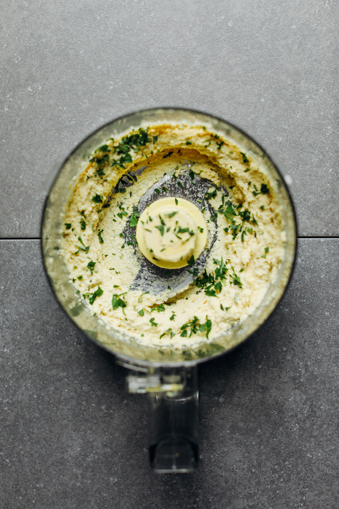 Food processor with freshly blended vegan Macadamia Nut Herb Cheese sprinkled with freshly chopped parsley