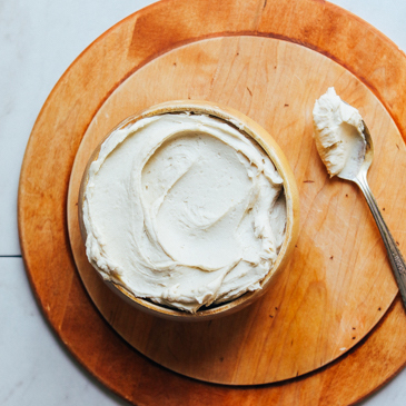 Spoon and bowl cashew buttercream frosting onto a wooden cutting board