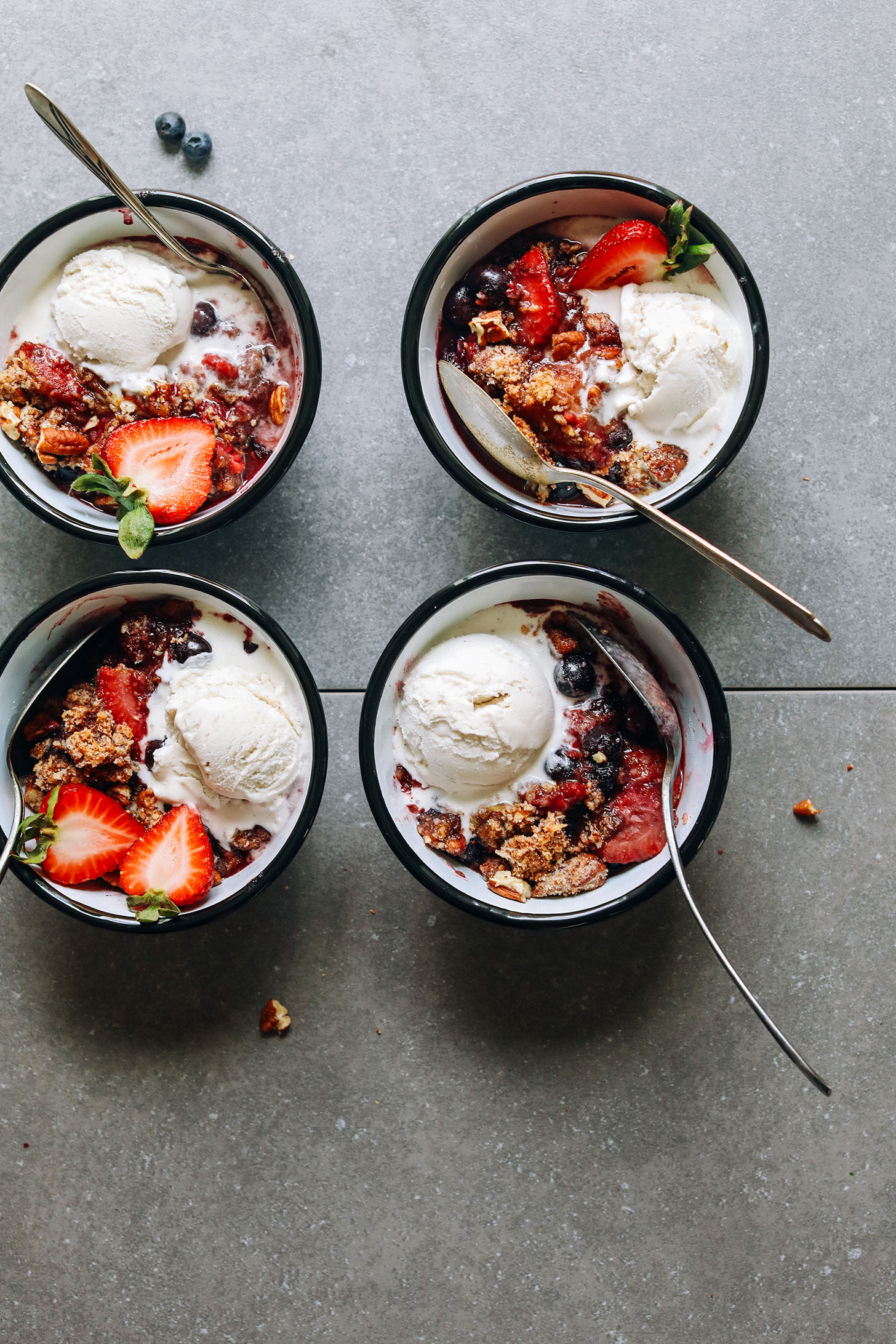 Four bowls of Grain-Free Berry Crisp with vegan ice cream and fresh strawberries