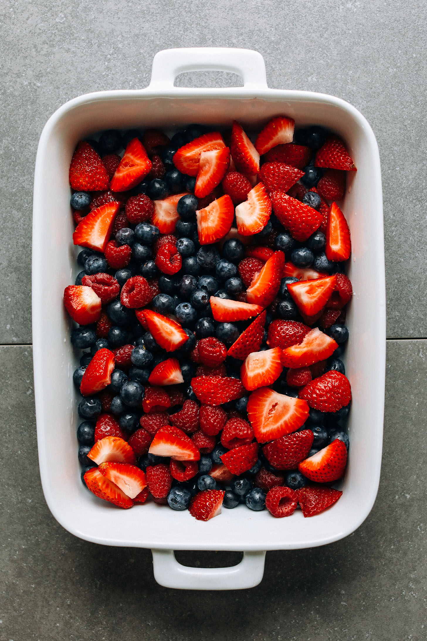 Fresh blueberries, raspberries, and strawberries in a ceramic baking dish