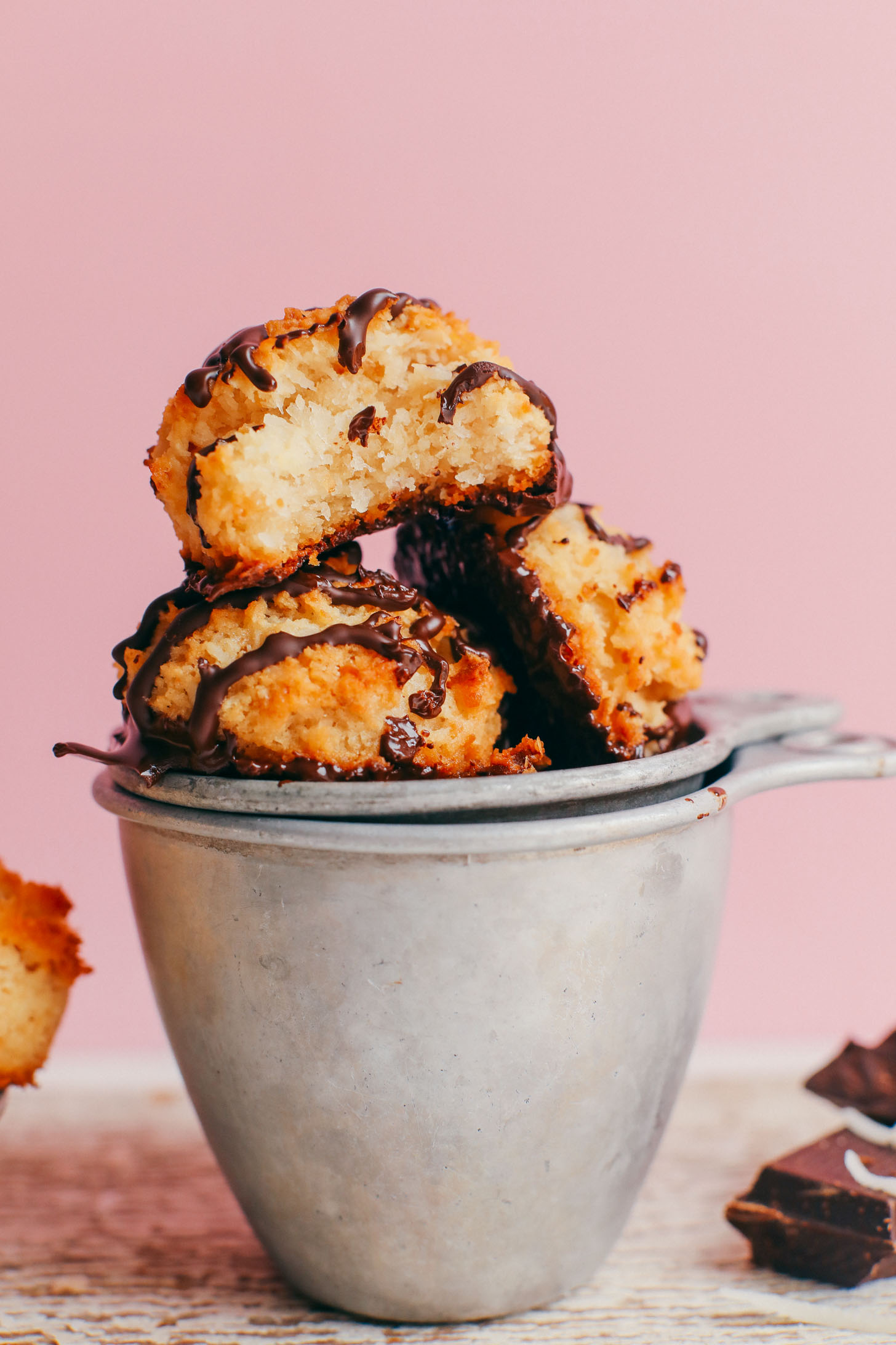 Crispy Vegan Macaroons with chocolate drizzle balanced on vintage measuring cups