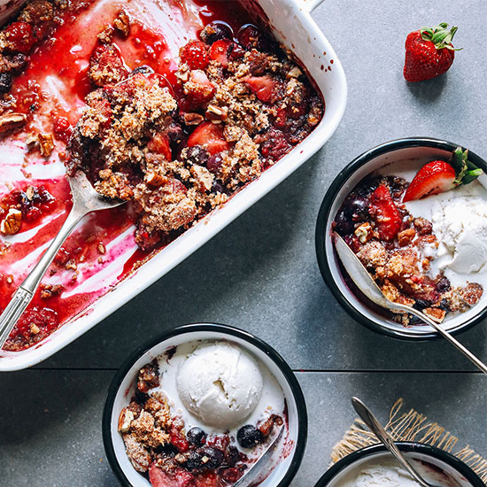 Two bowls and a baking pan of grain-free berry crisps served with vegan ice cream