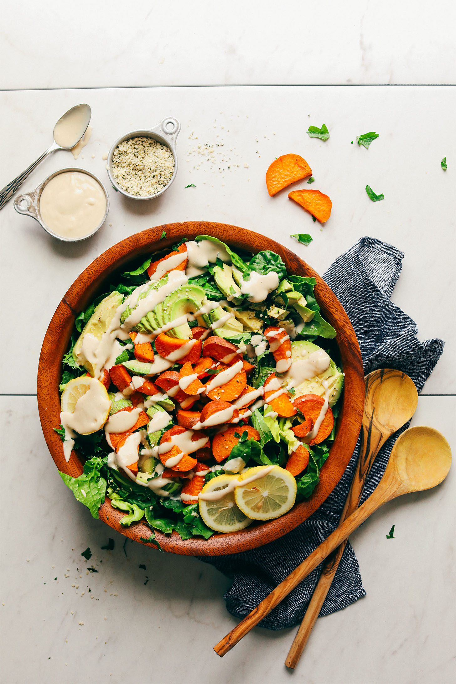Wood salad bowl filled with Healthy Sweet Potato Green Salad with avocado, hemp seeds, and tahini dressing