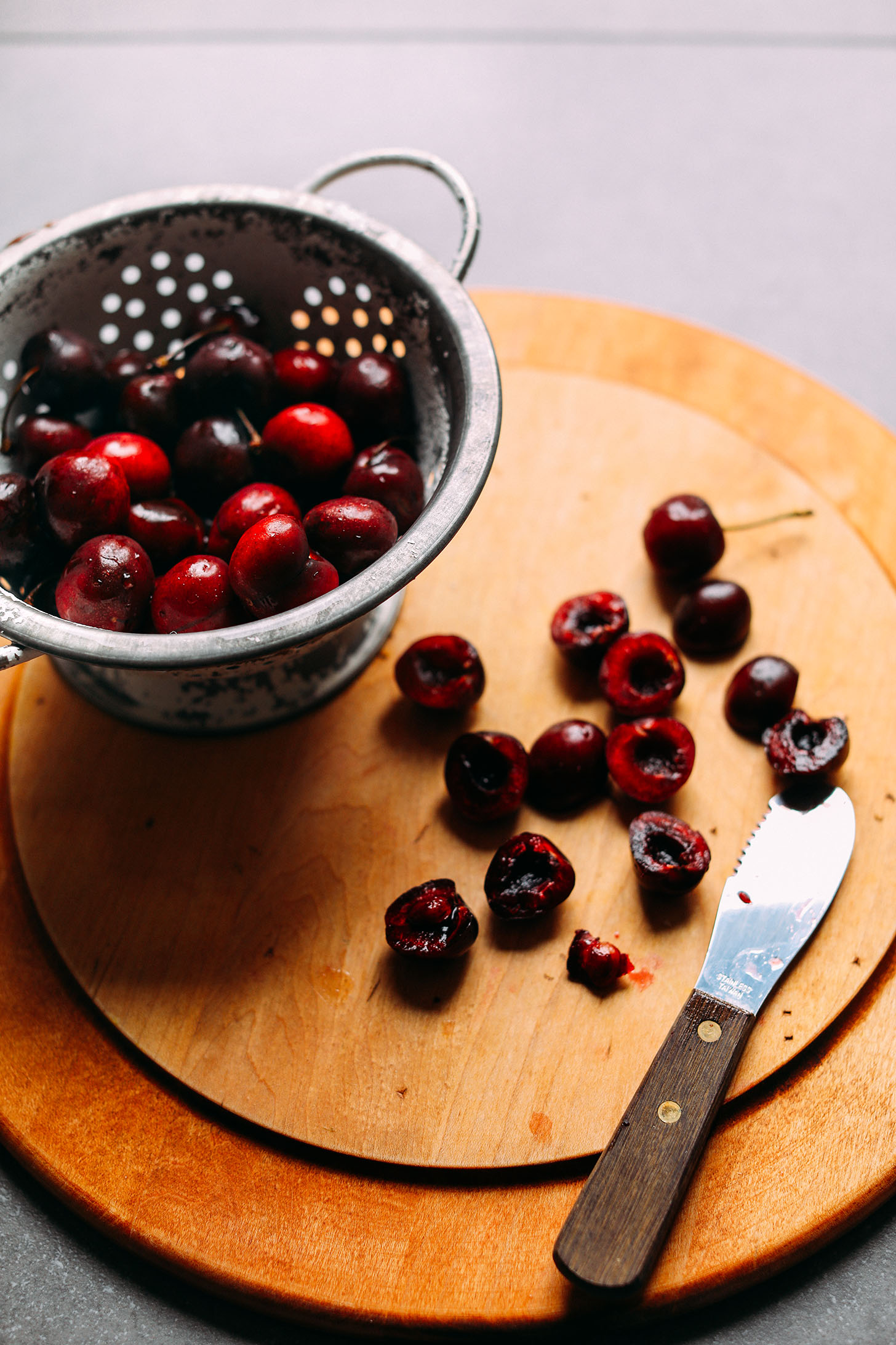 Colander with freshly washed cherries and some halved and pitted cherries on a wood cutting board