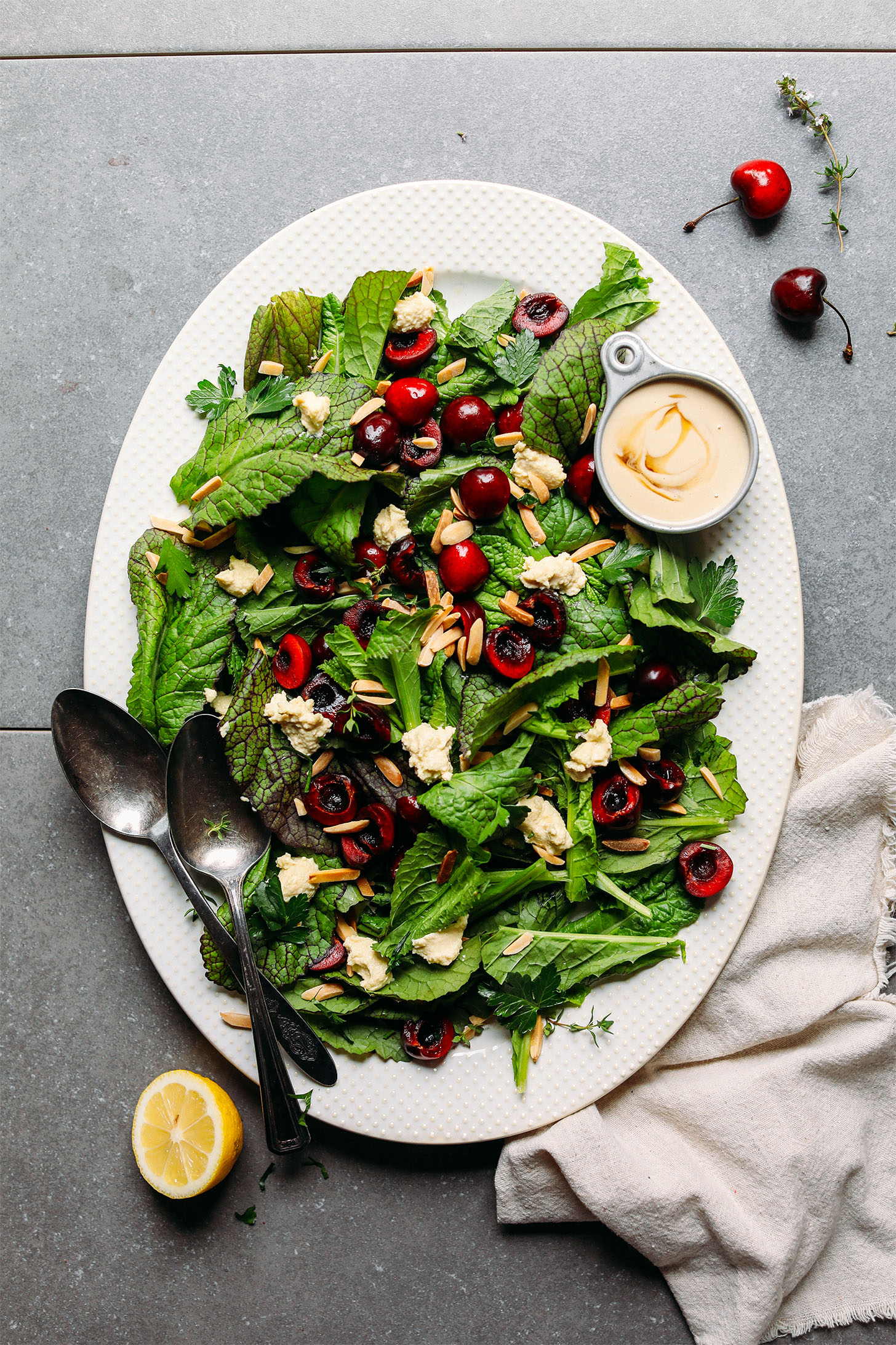 Large ceramic platter filled with healthy Mustard Green Salad with Cherries, Toasted Almonds, Nut Cheese, and Tahini Dressing