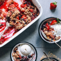 Baking dish and bowls of grain-free berry crisp with vanilla ice cream
