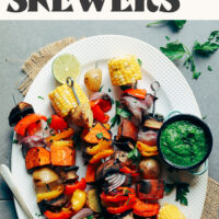 Platter of grilled veggie skewers with a bowl of herby green sauce