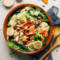 Wooden salad bowl filled with our Sweet Potato and Avocado Salad drizzled with tahini dressing