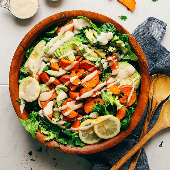 Wooden salad bowl filled with our sweet potato and avocado salad with tahini dressing