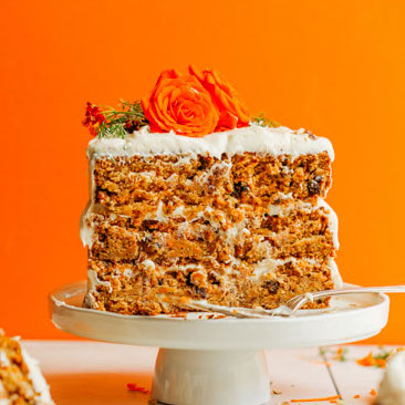 Cake platter with half of a Vegan GF Carrot Cake topped with Cashew Buttercream Frosting