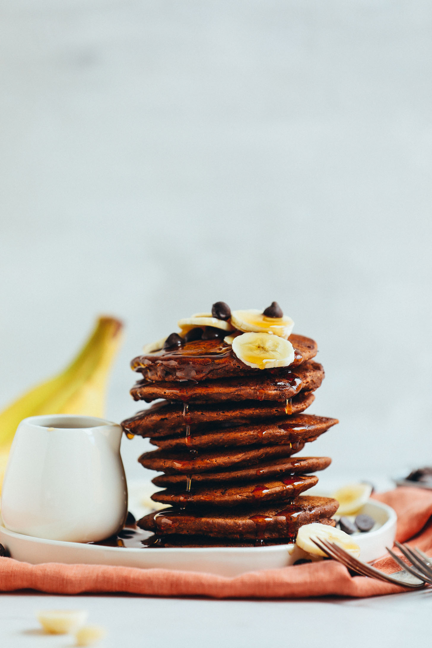 A stack of fluffy Vegan Chocolate Chocolate Chip Pancakes drizzled with syrup