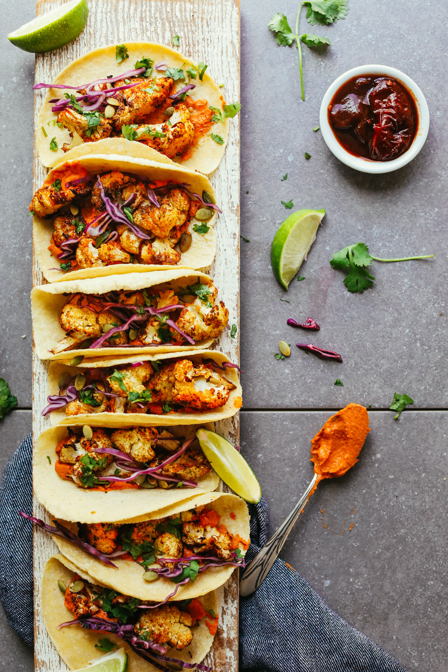 Wood plank with a line of gluten-free vegan Roasted Cauliflower Tacos with Adobo Romesco