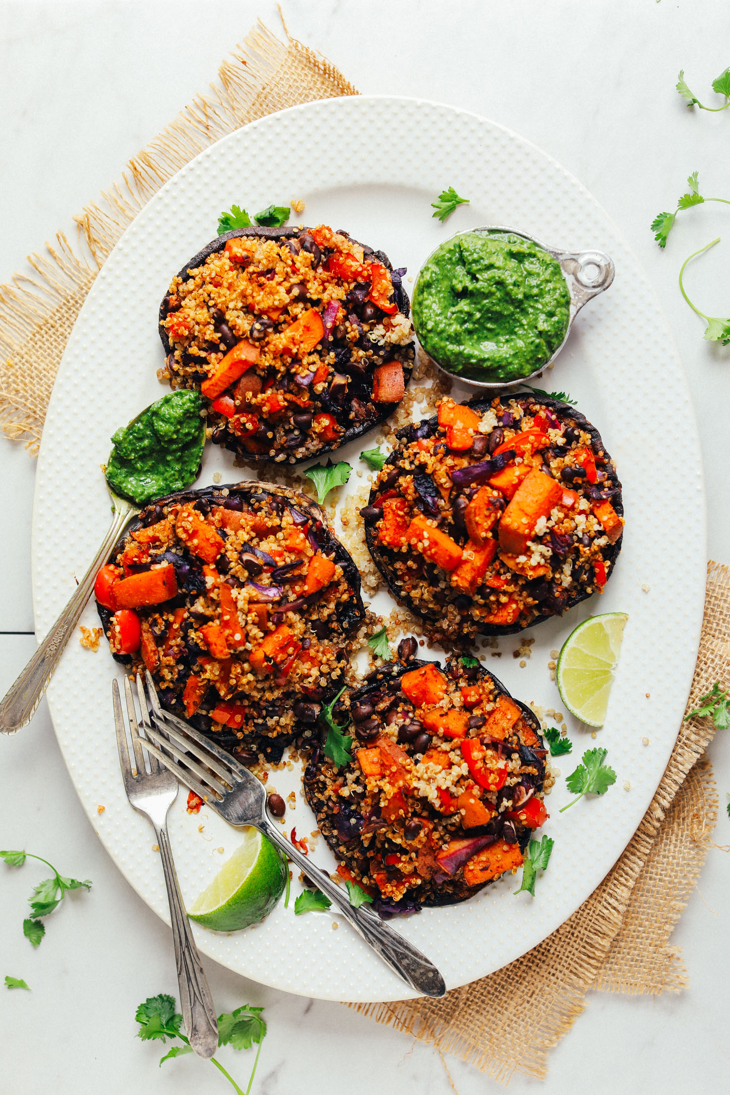 Four big Vegetable Quinoa Stuffed Portoballo Mushrooms on a large serving platter with a side of Chimichurri