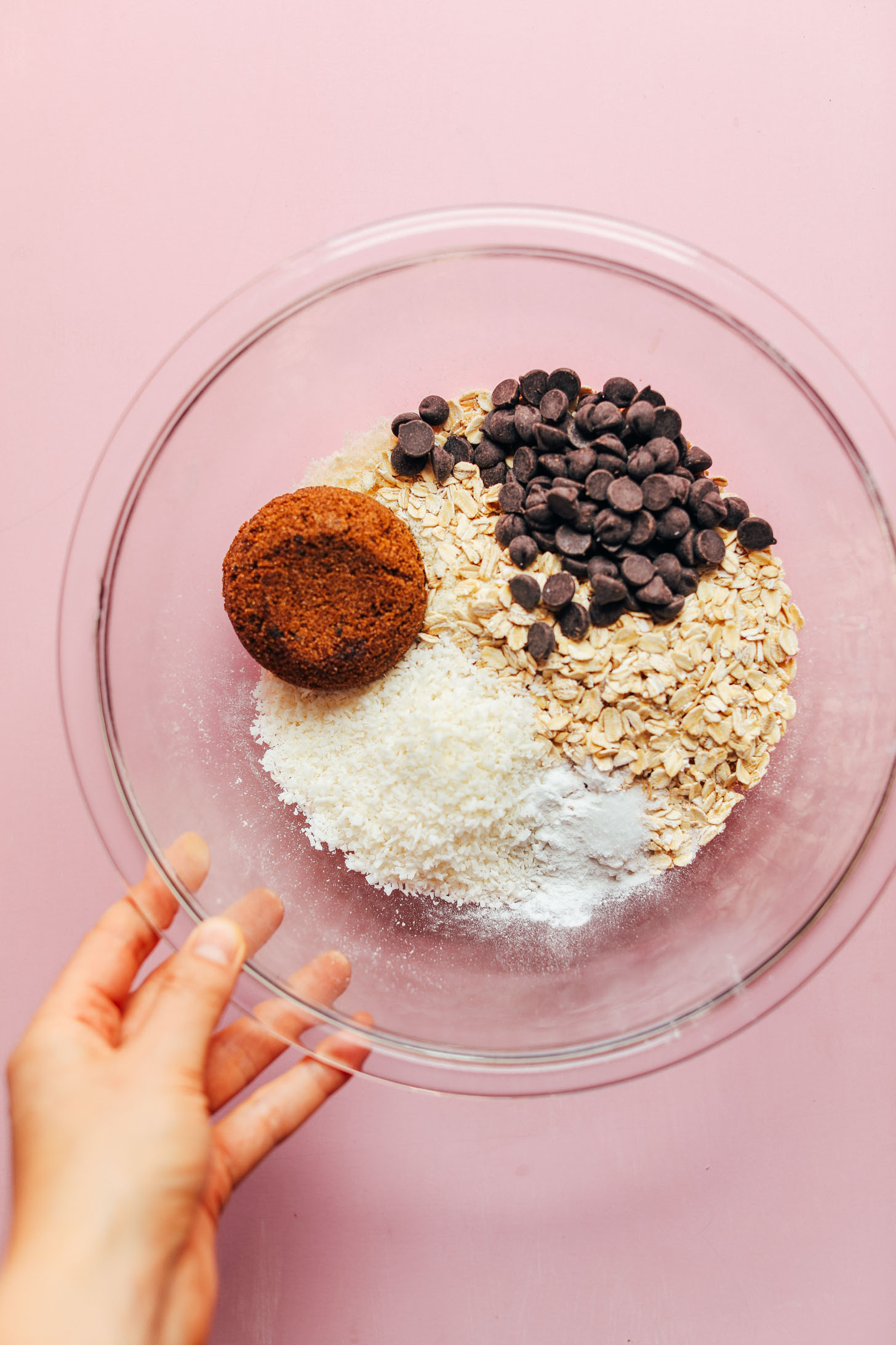 Glass mixing bowl with oats, almond flour, coconut sugar, dark chocolate chips, and other dry ingredients for Gluten-Free Oatmeal Chocolate Chip Cookies