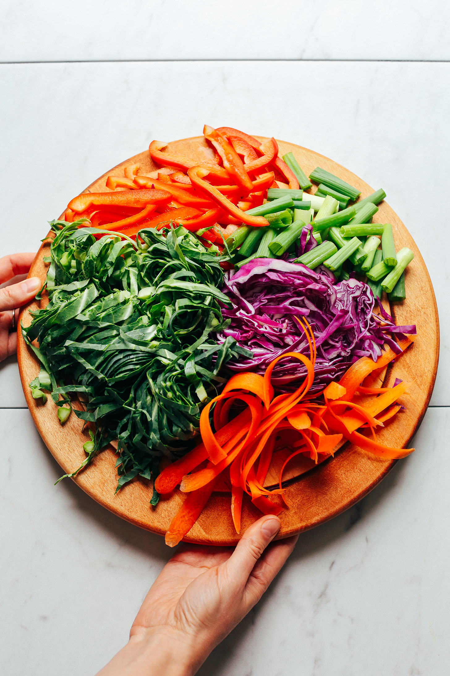 Wood cutting board with red bell pepper, collard greens, red cabbage, green onions, and carrots for making Noodle-Free Pad Thai