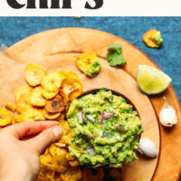 Dipping a crispy baked green plantain chip into a bowl of garlicky guacamole