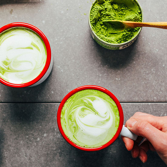 Container of matcha and two mugs of our Vegan Matcha Latte recipe