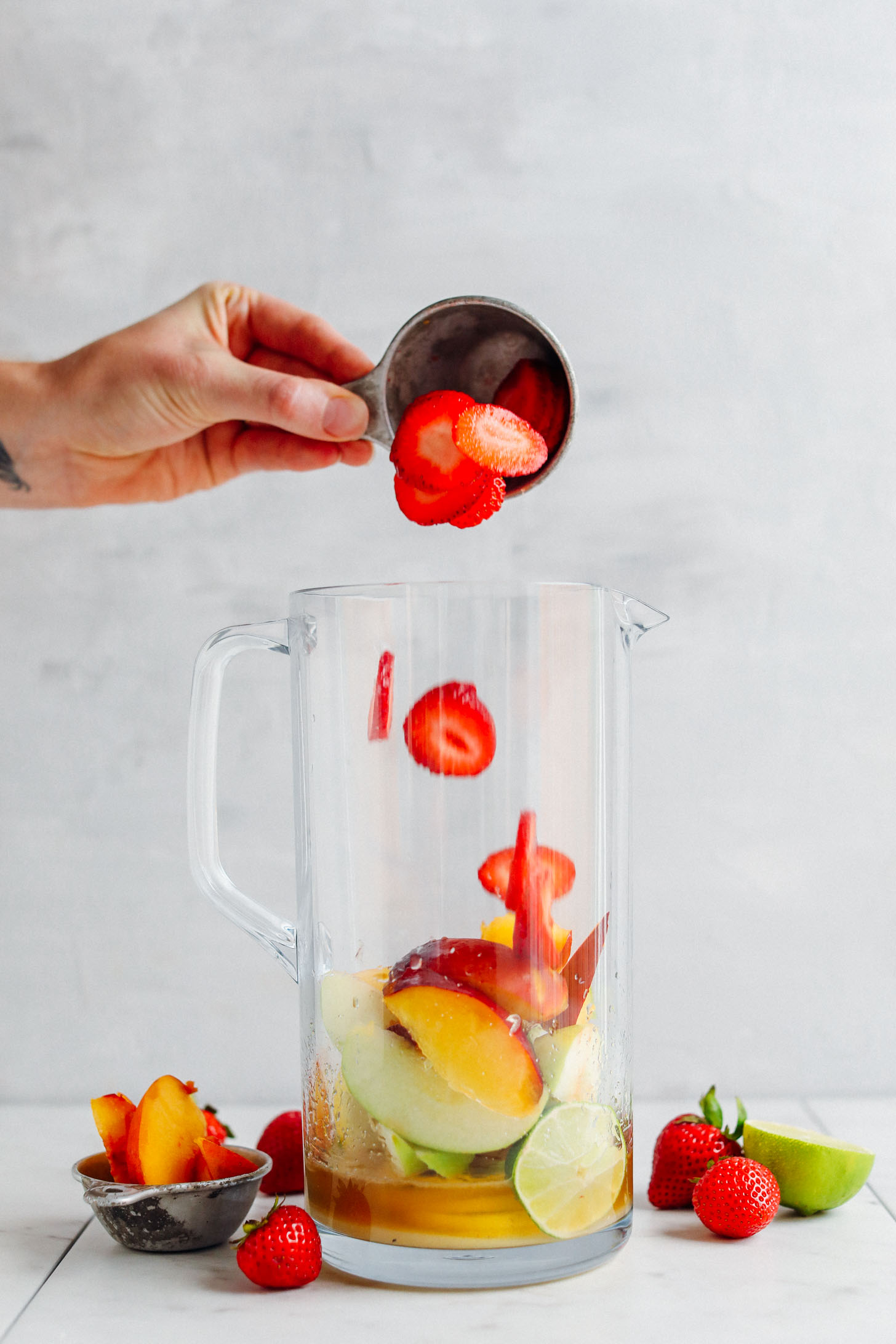Tossing strawberries into a pitcher with other fruit and apple brandy for an Easy Traditional White Sangria
