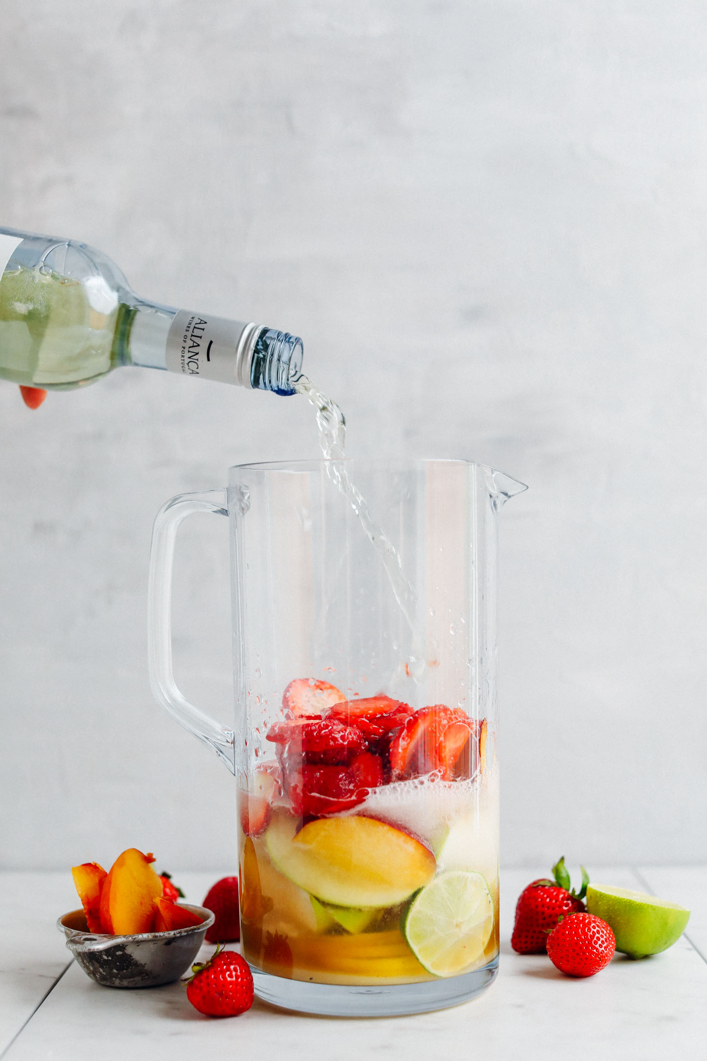 Pouring white wine into a pitcher of fresh summer fruits for Easy Traditional White Sangria