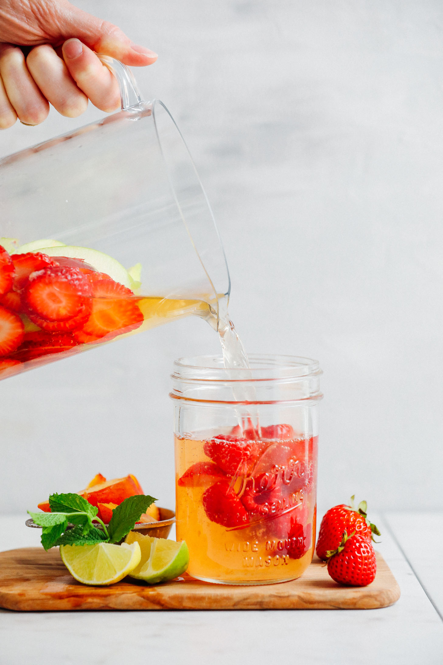 Pouring Easy Traditional White Sangria from a pitcher into a mason jar with fresh summer fruit