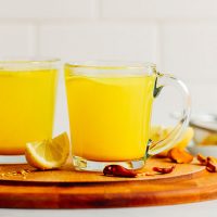 Two glass mugs of our Turmeric Tonic drink on a wood cutting board