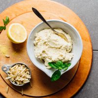 Bowl of whipped almond ricotta on a cutting board with slivered almonds and a lemon half
