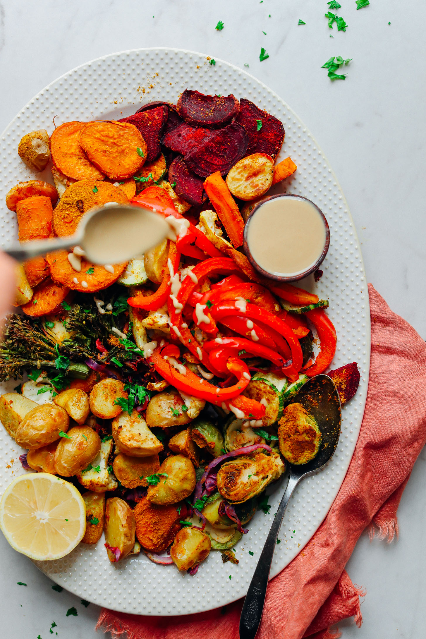 Drizzling tahini over a ceramic platter filled with Oil-Free Roasted Vegetables