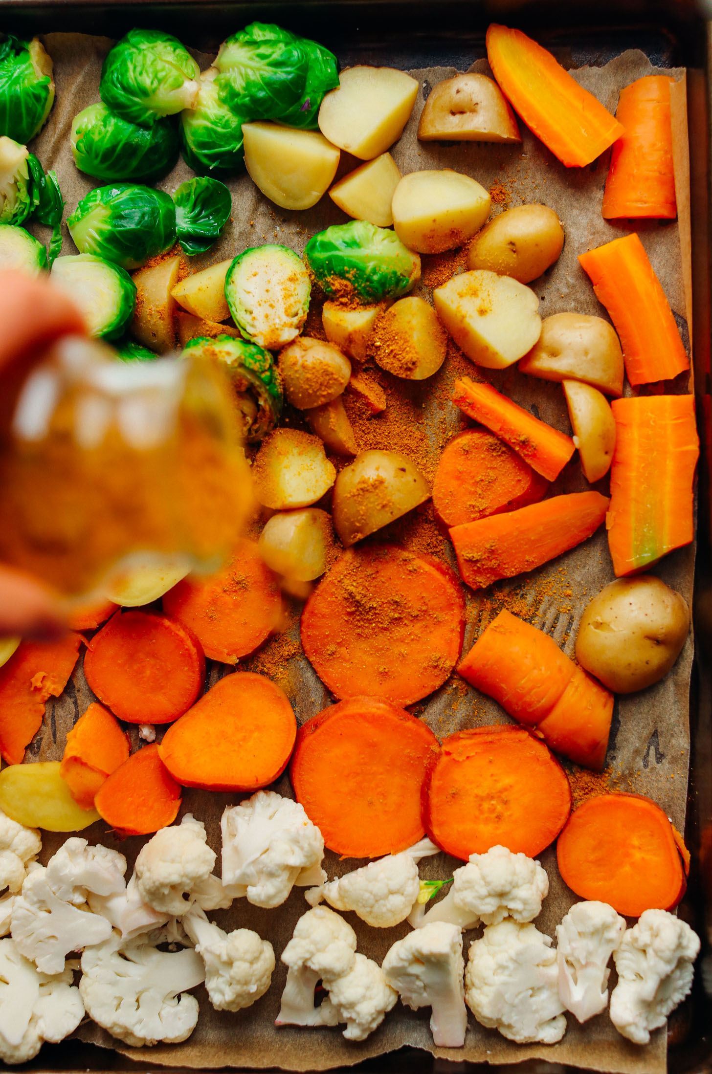 Sprinkling curry powder over a parchment-lined baking sheet filled with fresh veggies for roasting