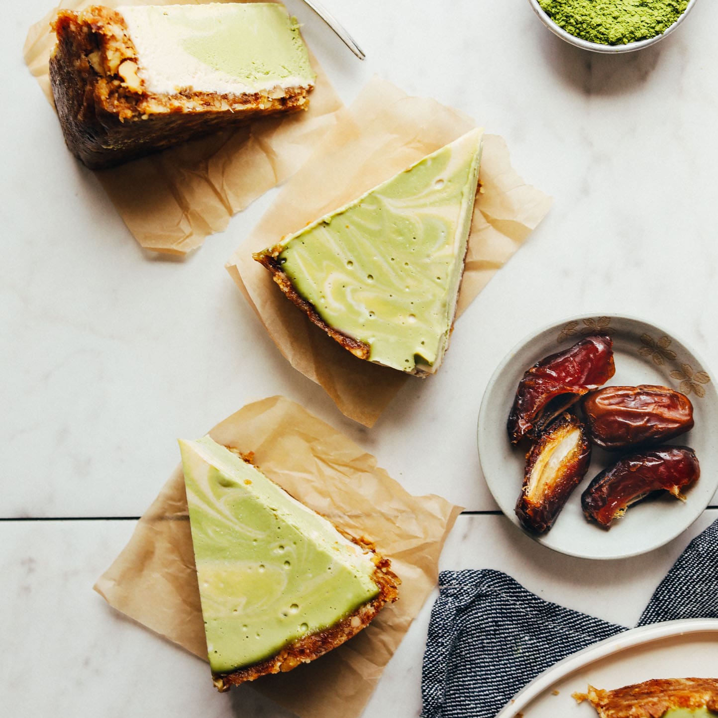 Slices of Vegan Matcha Cheesecake beside dates and matcha powder
